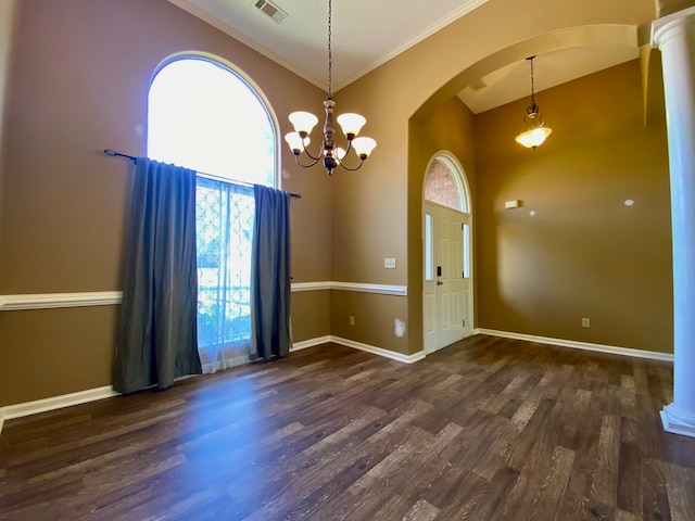 empty room with dark hardwood / wood-style floors, a towering ceiling, crown molding, and an inviting chandelier