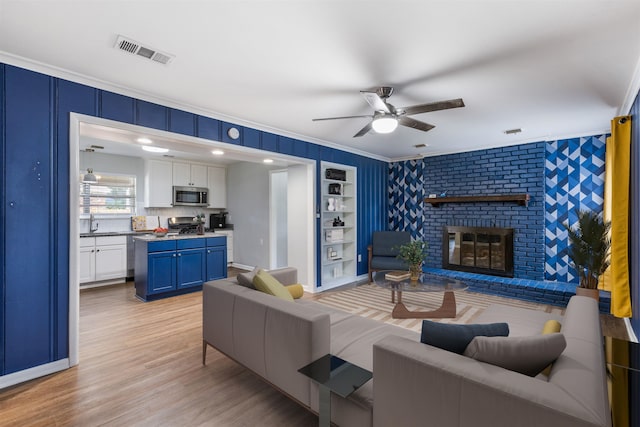 living room featuring light wood-type flooring, a brick fireplace, ornamental molding, built in shelves, and ceiling fan