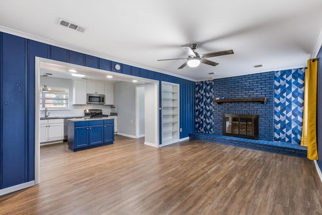 living room with a fireplace, light hardwood / wood-style floors, ceiling fan, and crown molding