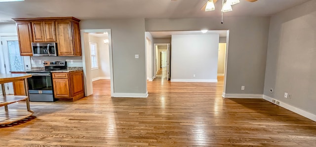 kitchen with light wood-type flooring, stainless steel appliances, light stone counters, and ceiling fan