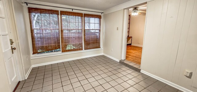 tiled spare room featuring ceiling fan, wood walls, and a textured ceiling