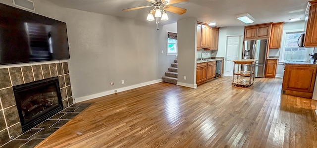 kitchen featuring appliances with stainless steel finishes, ceiling fan, sink, a tile fireplace, and wood-type flooring