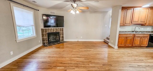 unfurnished living room featuring ceiling fan, light hardwood / wood-style floors, sink, and a fireplace