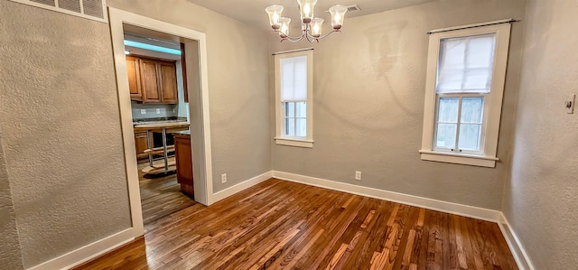 spare room with plenty of natural light, dark hardwood / wood-style flooring, and an inviting chandelier