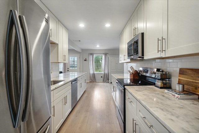 kitchen featuring white cabinetry, light hardwood / wood-style floors, light stone counters, and appliances with stainless steel finishes