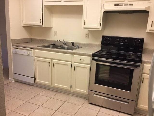 kitchen with stainless steel range with electric stovetop, white dishwasher, sink, light tile patterned floors, and white cabinetry