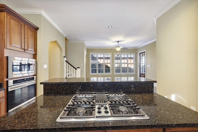 kitchen featuring kitchen peninsula, appliances with stainless steel finishes, ornamental molding, dark stone counters, and ceiling fan