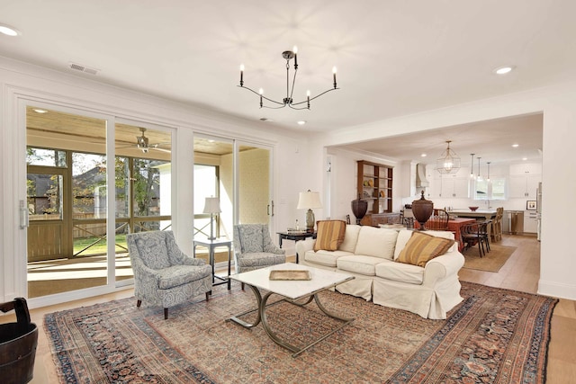 living room featuring ceiling fan with notable chandelier and light wood-type flooring