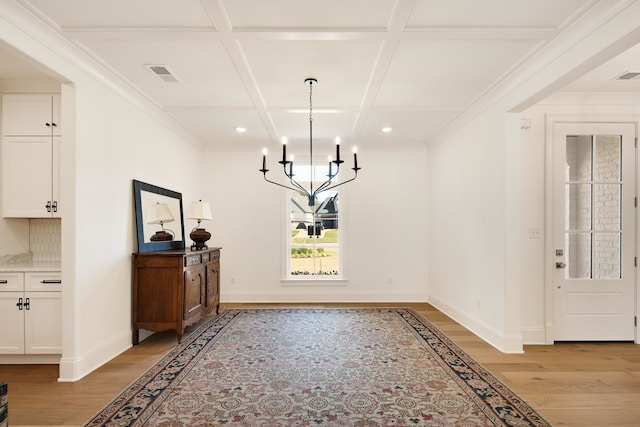 dining room with a chandelier, ornamental molding, light wood-type flooring, and coffered ceiling