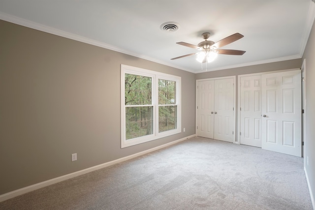 unfurnished bedroom featuring two closets, light colored carpet, ceiling fan, and crown molding