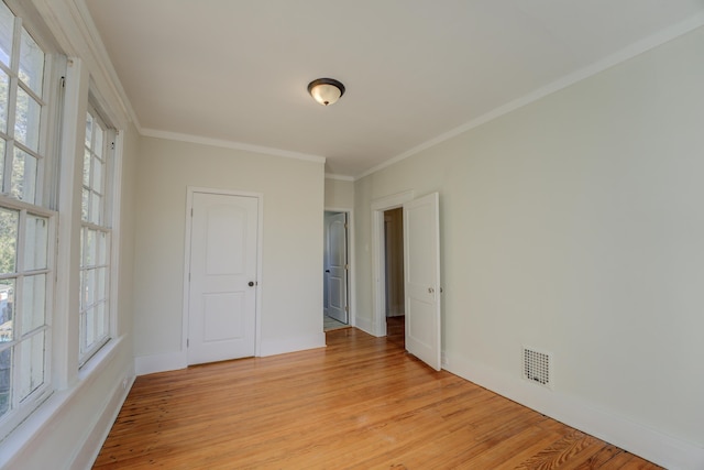 empty room featuring a wealth of natural light, ornamental molding, and light wood-type flooring