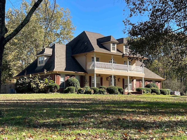 view of front facade with covered porch, central AC unit, a balcony, and a front yard