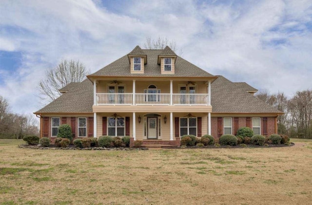 view of front of property with ceiling fan, a balcony, and a front yard