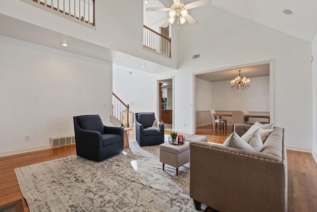 living room with wood-type flooring, ceiling fan with notable chandelier, and high vaulted ceiling