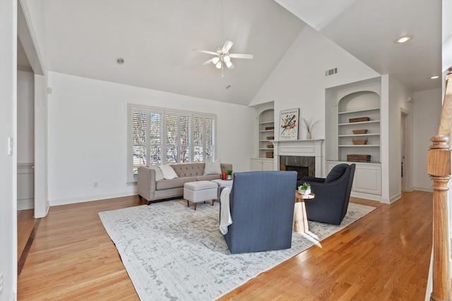 living room with ceiling fan, built in features, light wood-type flooring, and a tile fireplace