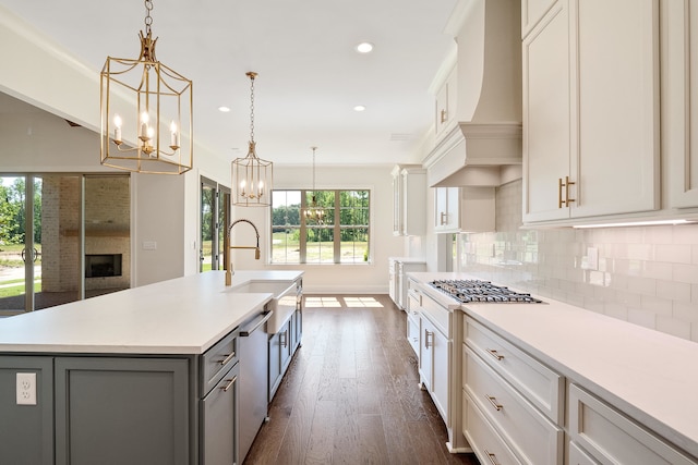 kitchen with appliances with stainless steel finishes, dark hardwood / wood-style flooring, custom range hood, a center island with sink, and decorative light fixtures