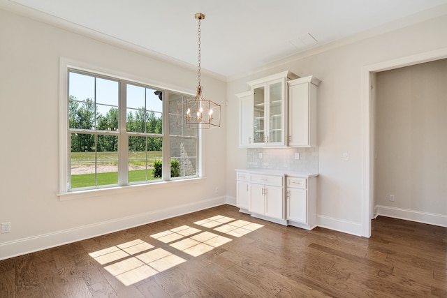 unfurnished dining area featuring dark hardwood / wood-style floors, ornamental molding, and a chandelier