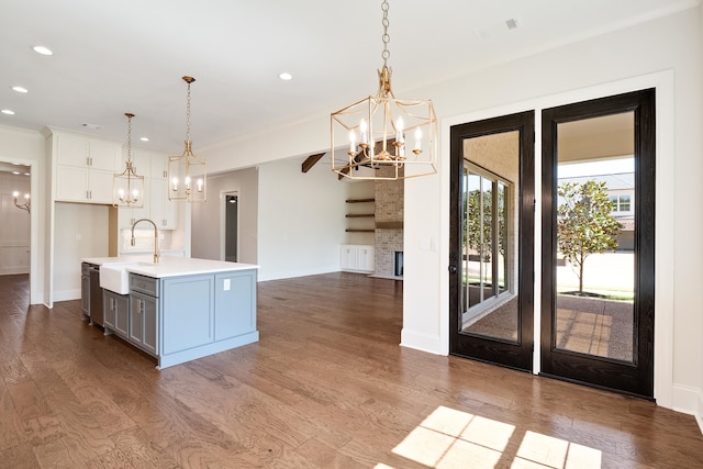 kitchen with hardwood / wood-style floors, decorative light fixtures, white cabinetry, and an island with sink