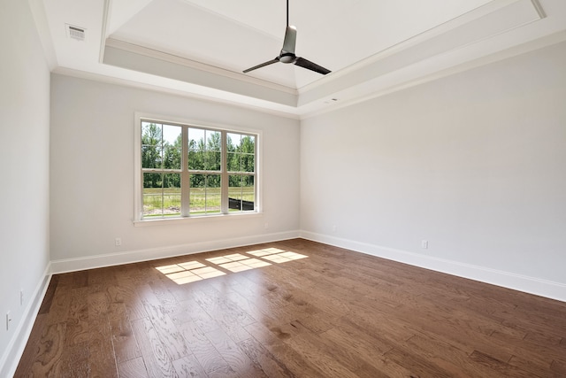 empty room featuring a raised ceiling, ceiling fan, dark wood-type flooring, and ornamental molding