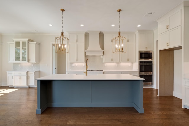 kitchen featuring dark hardwood / wood-style floors, custom range hood, a kitchen island with sink, and decorative light fixtures