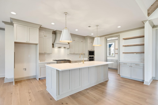 kitchen featuring custom range hood, decorative light fixtures, light hardwood / wood-style floors, and an island with sink