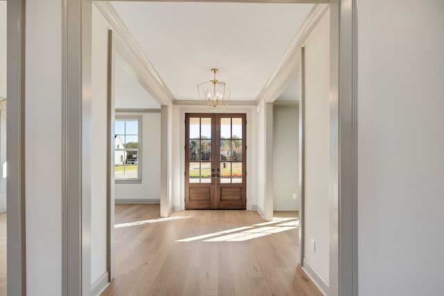 foyer entrance with ornamental molding, french doors, a chandelier, and light hardwood / wood-style flooring