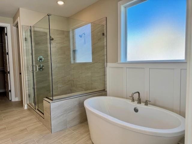 full bath with a freestanding tub, a shower stall, a decorative wall, and wainscoting