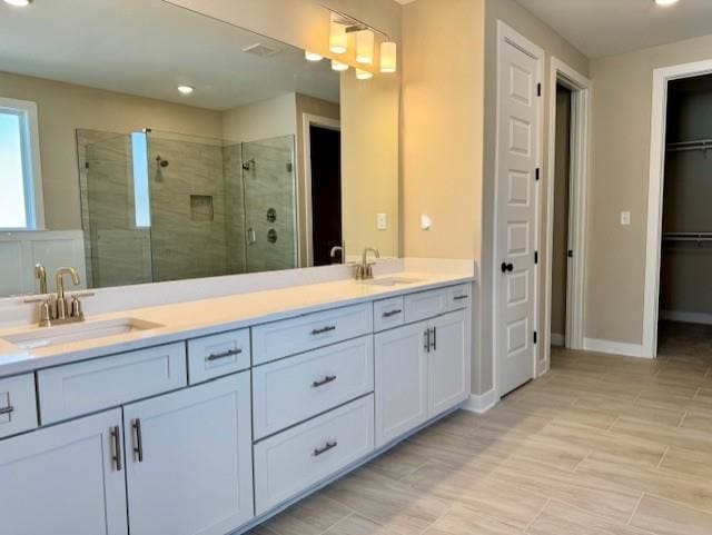 bathroom with a walk in closet, a sink, a shower stall, and double vanity