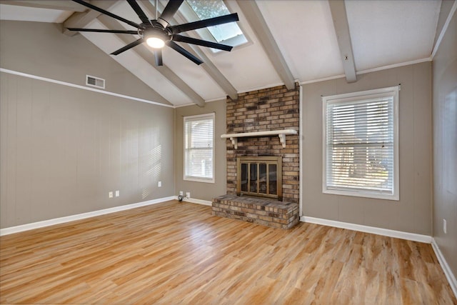 unfurnished living room featuring a brick fireplace, vaulted ceiling with skylight, ceiling fan, crown molding, and light hardwood / wood-style flooring