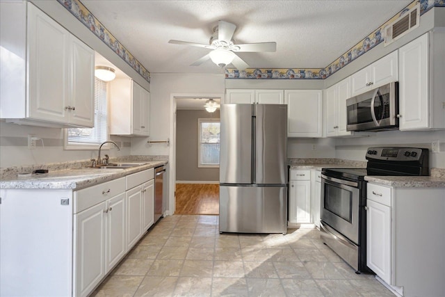 kitchen with sink, ceiling fan, a textured ceiling, appliances with stainless steel finishes, and white cabinetry