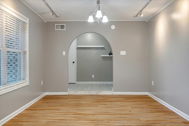 empty room featuring ornamental molding, rail lighting, light hardwood / wood-style floors, and an inviting chandelier