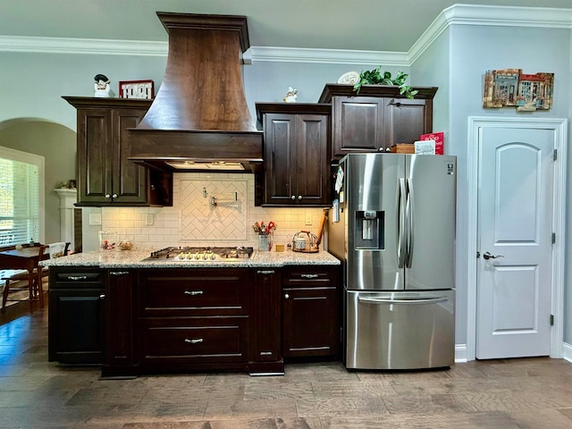 kitchen featuring dark brown cabinets, custom range hood, ornamental molding, and appliances with stainless steel finishes