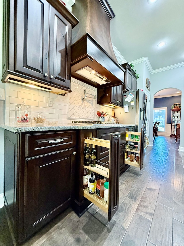 kitchen featuring premium range hood, wood-type flooring, ornamental molding, tasteful backsplash, and dark brown cabinetry