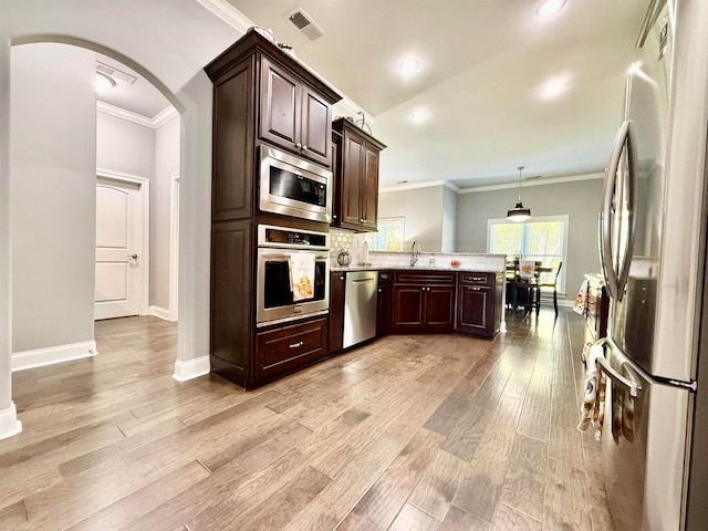 kitchen with kitchen peninsula, light wood-type flooring, ornamental molding, stainless steel appliances, and decorative light fixtures