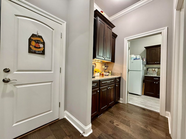 bar featuring dark wood-type flooring, white refrigerator, crown molding, light stone countertops, and dark brown cabinetry