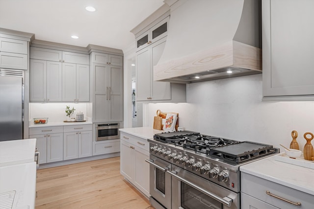 kitchen with gray cabinetry, custom exhaust hood, high end appliances, and light wood-type flooring