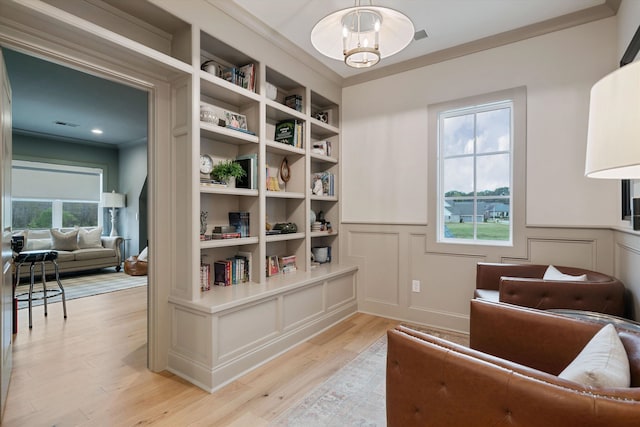 sitting room with a wealth of natural light, ornamental molding, and light wood-type flooring