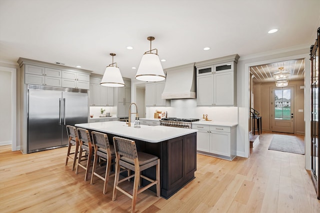 kitchen featuring hanging light fixtures, stainless steel appliances, light hardwood / wood-style floors, custom exhaust hood, and ornamental molding