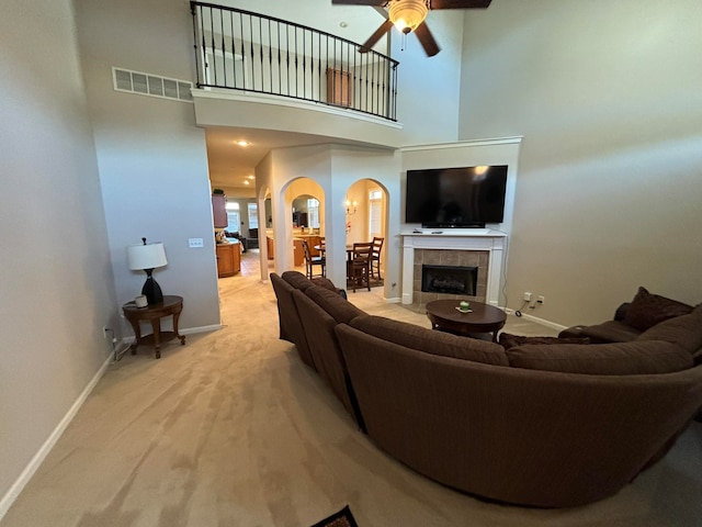 carpeted living room featuring a tile fireplace, a towering ceiling, and ceiling fan