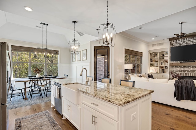 kitchen with built in shelves, a kitchen island with sink, hanging light fixtures, and appliances with stainless steel finishes