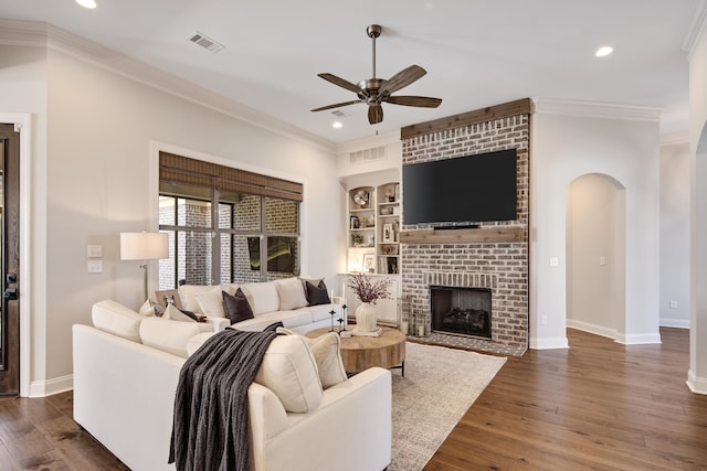 living room with ceiling fan, a brick fireplace, dark hardwood / wood-style flooring, built in features, and ornamental molding