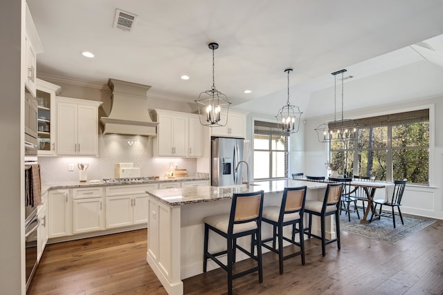 kitchen featuring premium range hood, a kitchen island with sink, white cabinets, and stainless steel appliances