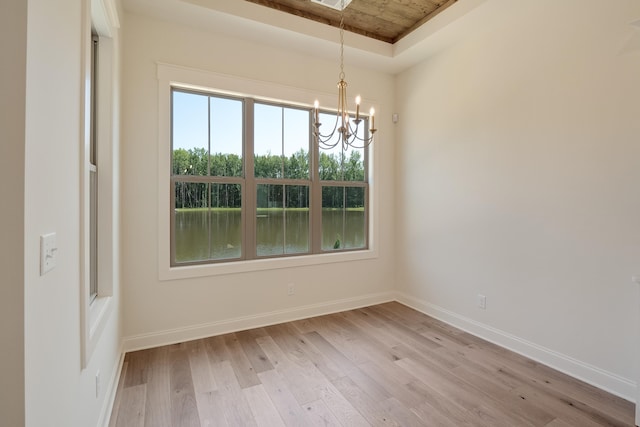 unfurnished dining area featuring an inviting chandelier, a raised ceiling, a water view, and light hardwood / wood-style flooring