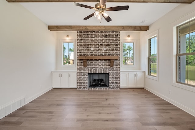 unfurnished living room with beamed ceiling, hardwood / wood-style floors, a brick fireplace, and ceiling fan