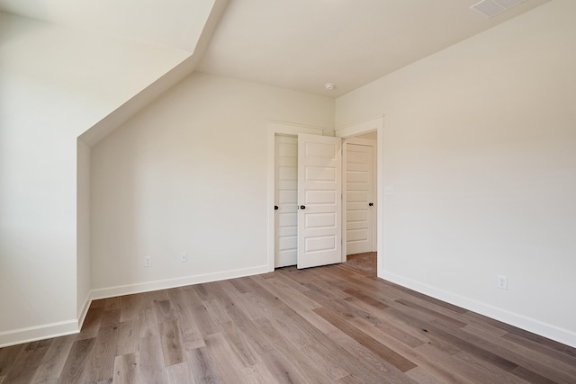 unfurnished bedroom with light wood-type flooring and vaulted ceiling