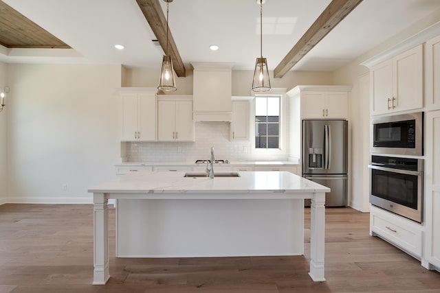 kitchen featuring beamed ceiling, stainless steel appliances, a center island with sink, and light hardwood / wood-style floors