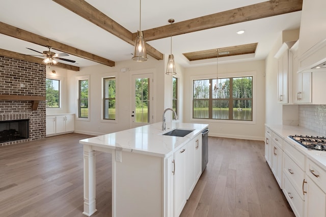 kitchen featuring sink, pendant lighting, a center island with sink, white cabinets, and light hardwood / wood-style floors