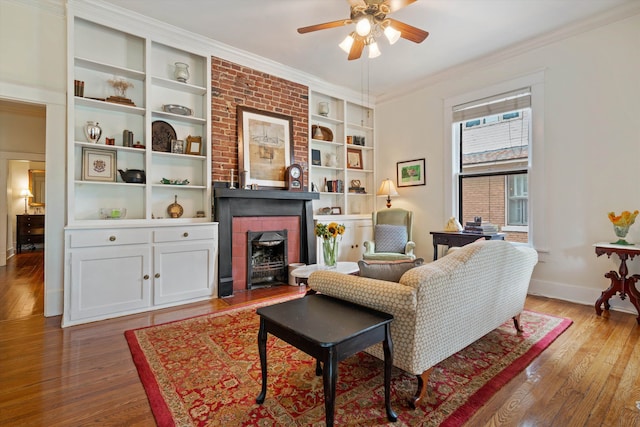 living area featuring crown molding, ceiling fan, built in shelves, a large fireplace, and wood-type flooring