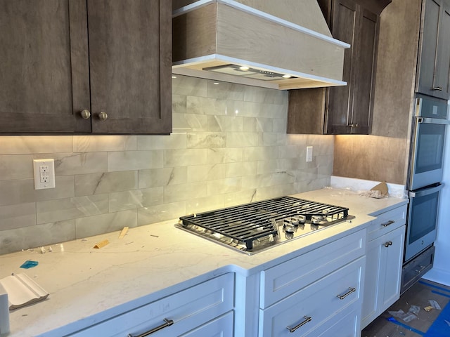 kitchen featuring light stone counters, stainless steel appliances, backsplash, dark brown cabinetry, and premium range hood