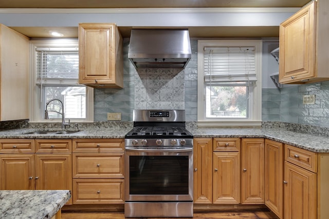 kitchen featuring sink, wall chimney range hood, stainless steel gas range oven, light stone counters, and wood-type flooring